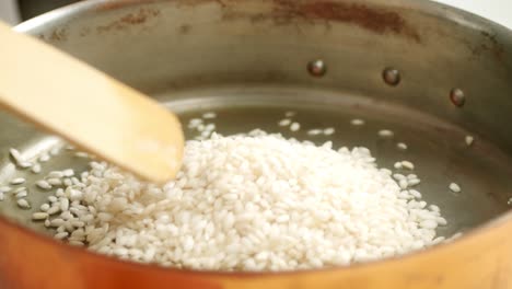 cook pouring rice into pan while preparing dish