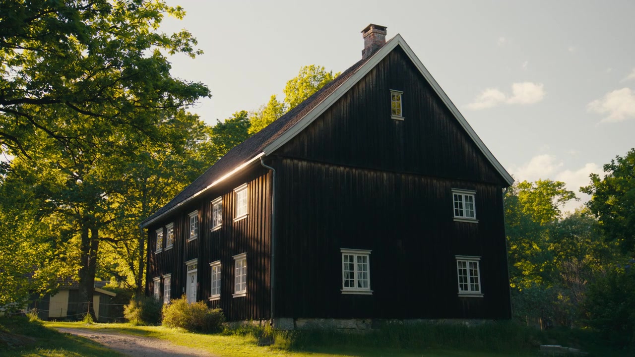 Ett historiskt skolhus i trä står i varmt kvällssolsken bland tysta träd, där traditionell arkitektur, mjuka skuggor och lugna lantliga omgivningar skapar en tidlös scen rik på kulturarv