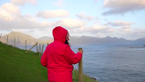 mujer con chaqueta de capucha roja agarrándose al palo debido al fuerte viento en gjogv, islas feroe