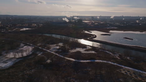 meandering river with industrial backdrop, winter tones, late afternoon light, aerial view
