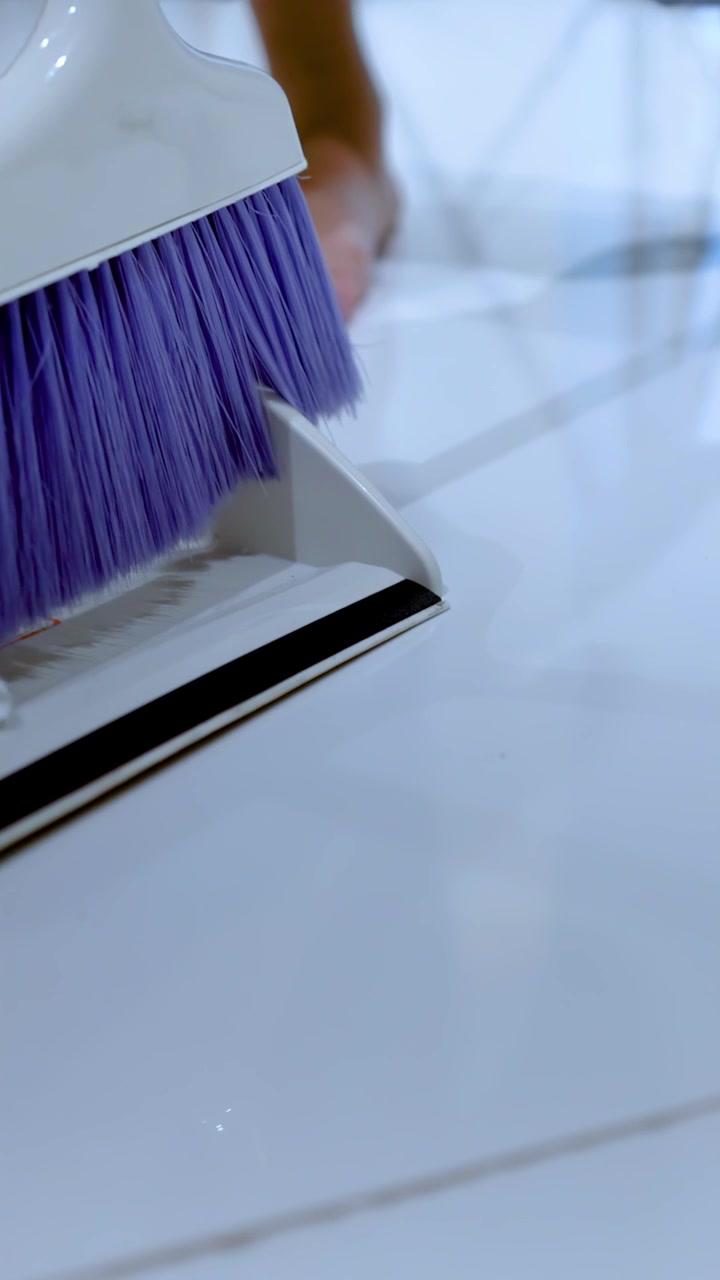 Person Sweeping Debris into Dustpan on Tiled Floor