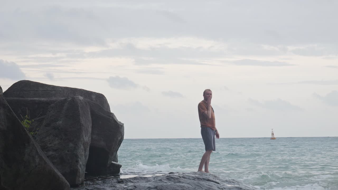 hombre gracioso haciendo una pose y luego soplando un beso a la cámara mientras estaba de pie en la roca