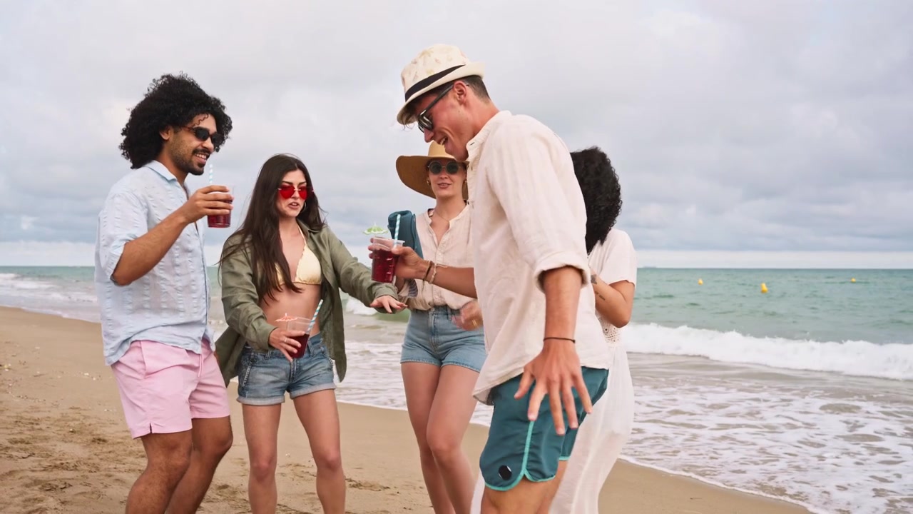 Giovani amici felici che ballano e bevono cocktail sulla spiaggia
