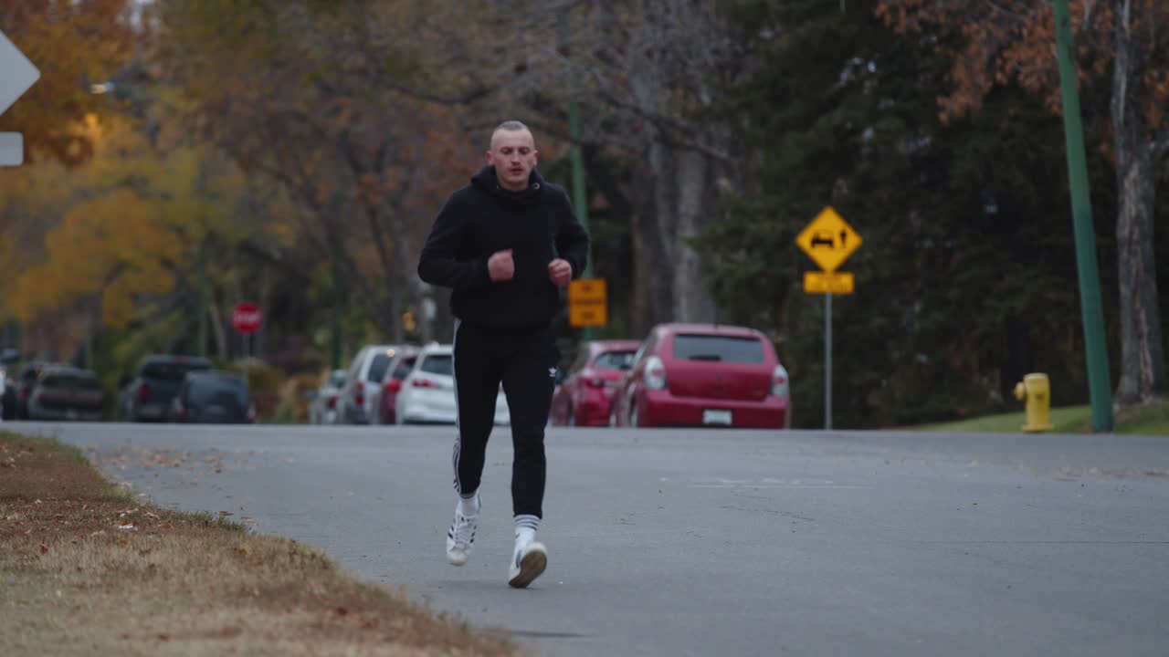 Man running down a road through a neighborhood with green trees and street signs