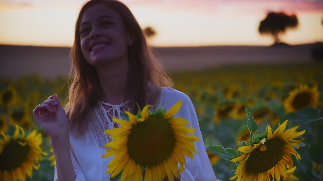 una chica guapa sonriente arranca un pétalo de girasol y mira hacia arriba para pedir un deseo, plano medio