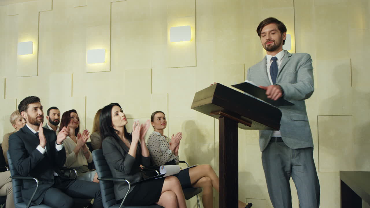кавказский молодой бизнесмен входит в конференц-зал, люди хлопают, затем он поднимается на подиум