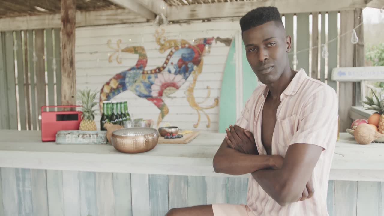 retrato de un feliz hombre afroamericano sentado y sonriendo en un bar de la playa, en cámara lenta.