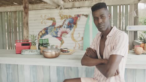 Portrait-of-happy-african-american-man-sitting-and-smiling-at-a-beach-bar,-slow-motion