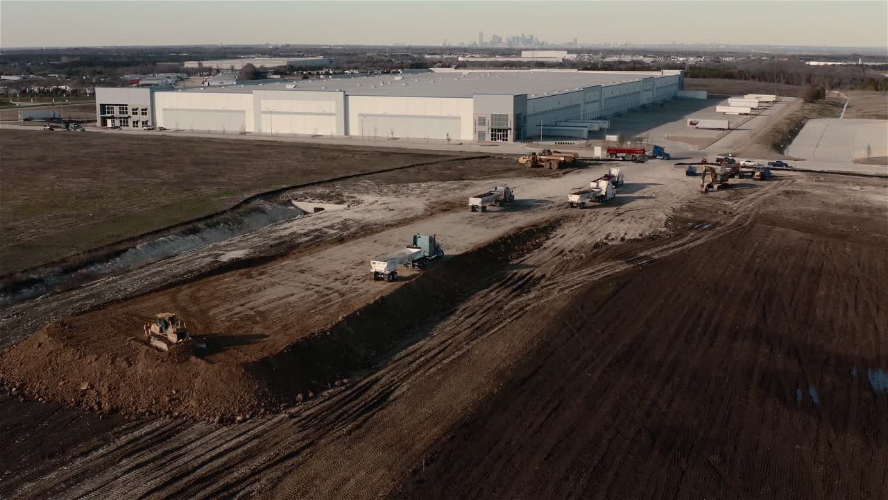 On a construction site, dump trucks and a catepillar tractor build up the dirt for a new building foundation.