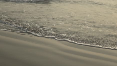 Las-Suaves-Olas-Rompen-Contra-Una-Playa-De-Arena-Al-Anochecer,-Creando-Serenas-Ondas-Y-Patrones-En-La-Arena.