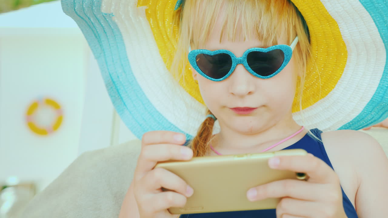The Child Relaxes After Swimming In The Pool - Plays On The Smartphone