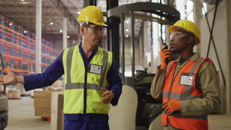 diverse male workers wearing safety suits and talking in warehouse