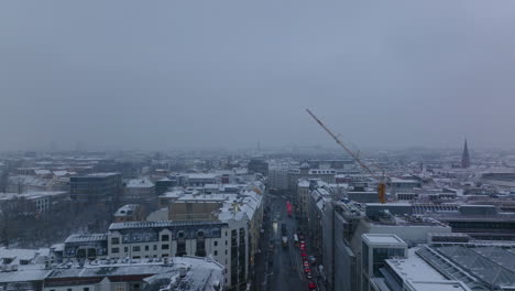 Forwards-fly-above-street-in-city.-Cars-standing-on-road-at-crossroads.-Winter-atmosphere-with-snow-dusted-roofs.-Berlin,-Germany