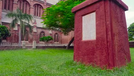 A-low-angle-aerial-view-of-a-beautiful-old-Church-made-with-red-bricks,-Green-grass-and-trees-in-the-Church