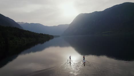 Drohnenaufnahme-über-Dem-Bohinjer-See-In-Slowenien,-Während-Ein-Paar-Abends-Stand-Up-Paddeln-Mit-Bergen-Im-Hintergrund-Macht