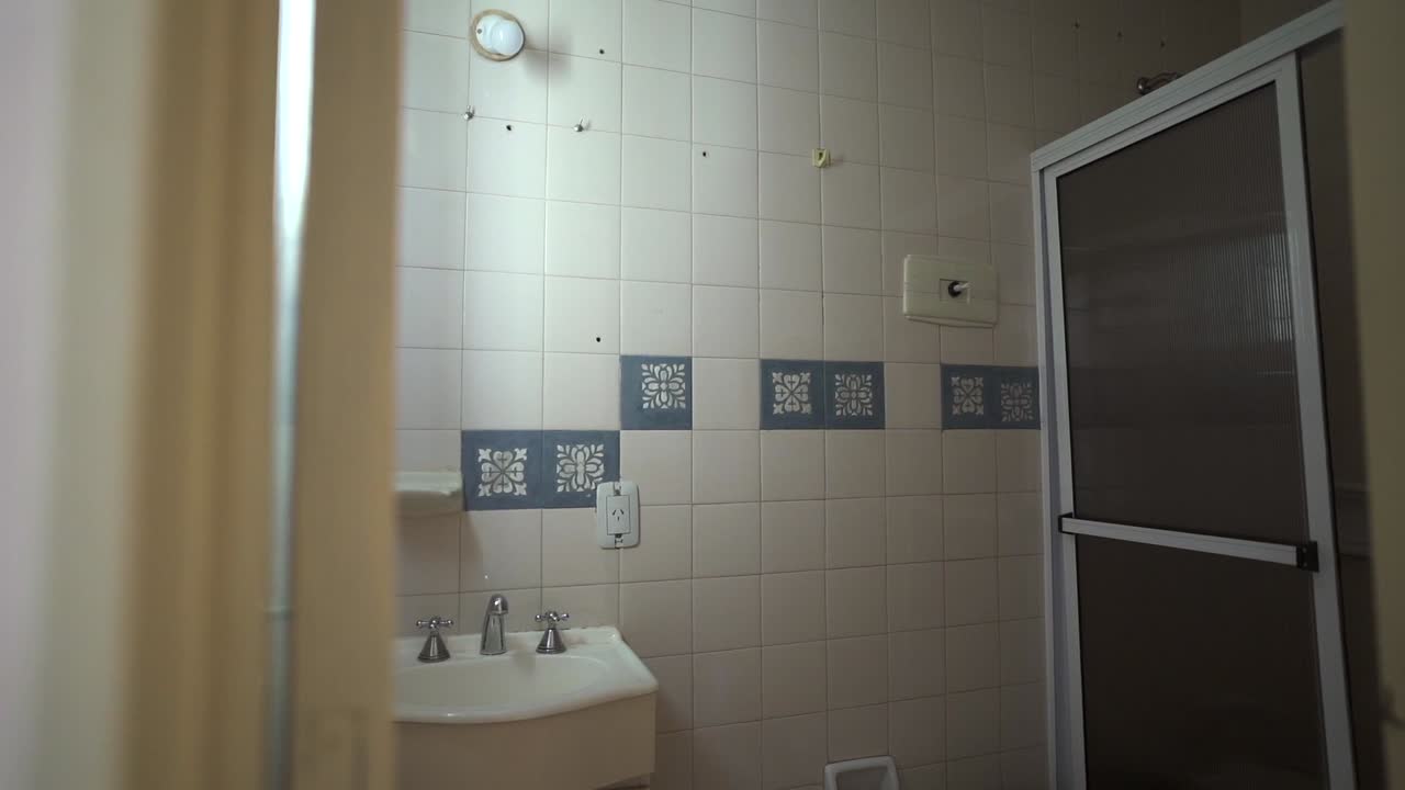 Modern modest bathroom with white square tiles, blue patterned accents, and a framed glass shower door, minimal and clean space, soft indoor light, slow reveal shot, no people