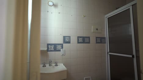 Modern modest bathroom with white square tiles, blue patterned accents, and a framed glass shower door, minimal and clean space, soft indoor light, slow reveal shot, no people