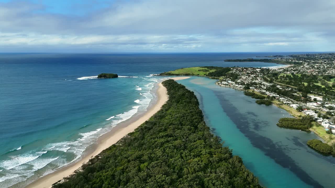 Aerial of Minnamurra River mouth meeting Pacific Ocean along sandy coastline in NSW, Australia, white sand contrasts urban development and forest