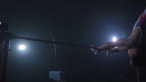 gimnasta en un fondo oscuro en la barra transversal realiza giros y salta sobre sí mismo en el aire en cámara lenta y alrededor del humo