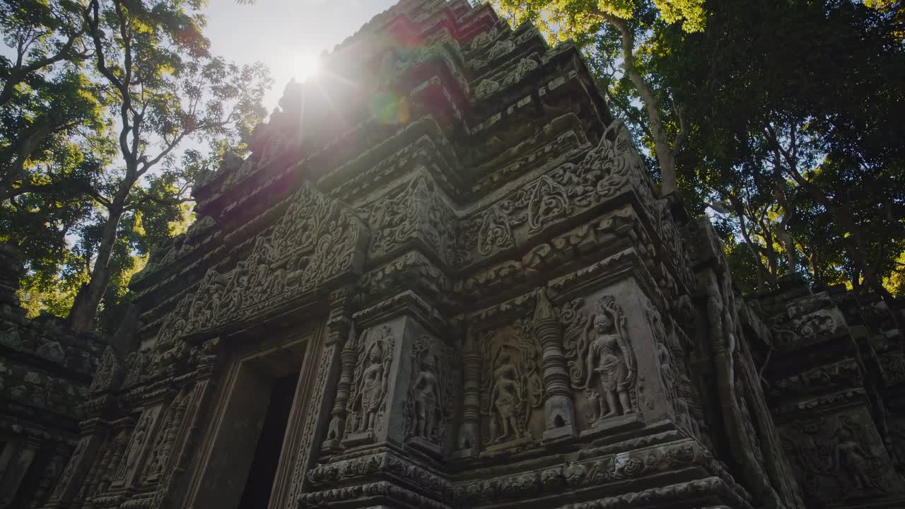 Low-angle video shot of ancient temple ruins surrounded by lush trees, capturing intricate carvings