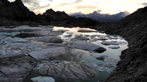 Vista-Aérea-De-Icebergs-En-El-Lago-Glaciar-Derritiéndose-En-Partes-Remotas-De-Los-Alpes-Suizos-Con-El-Resplandor-Del-Atardecer-Reflejándose-En-El-Agua