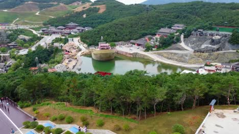 aerial panorama shot of huaxiacheng theme park in weihai china with view of visitors and tourists and various attractions, lakes and a bridge amidst a beautiful landscape