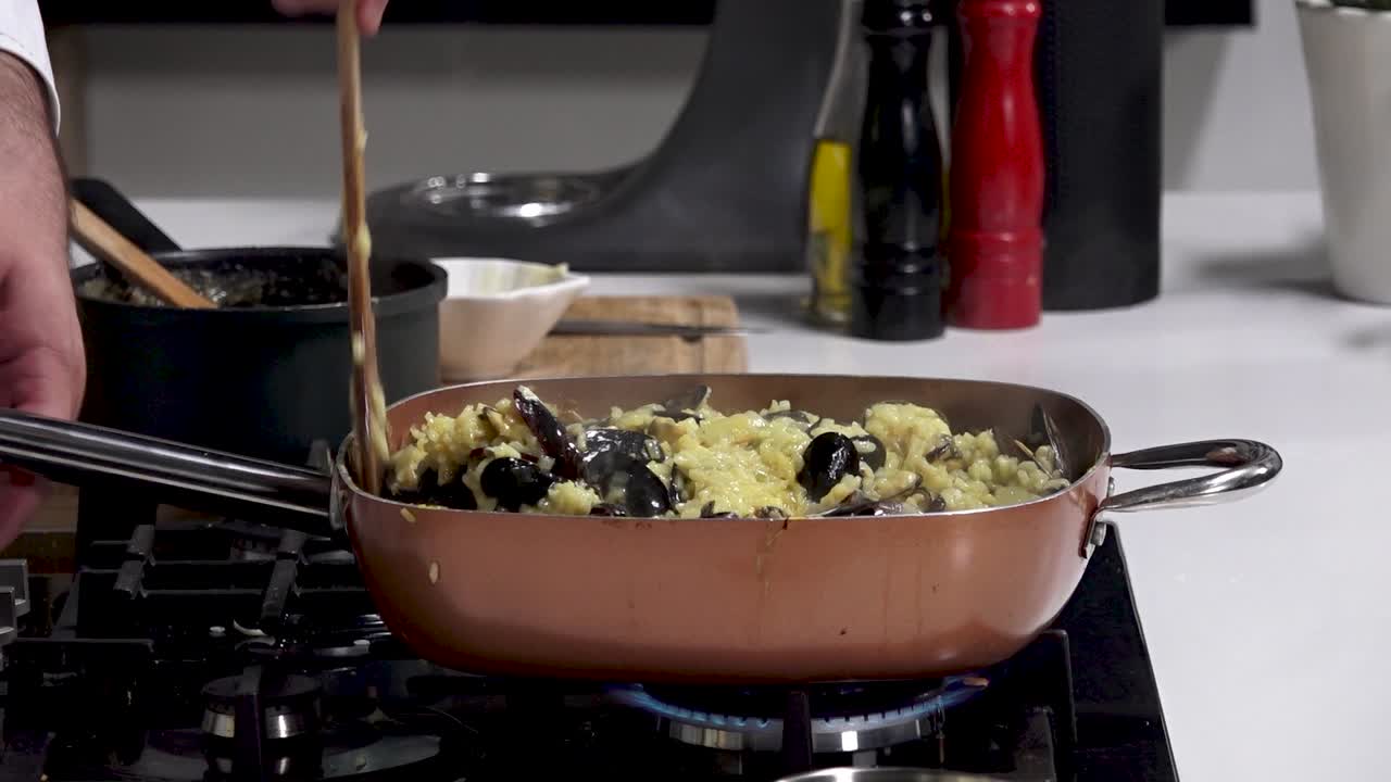 In a contemporary kitchen, fresh mussels are added to a creamy pasta dish, stirred together on a stovetop. Aromas fill the air as dinner is prepared with care