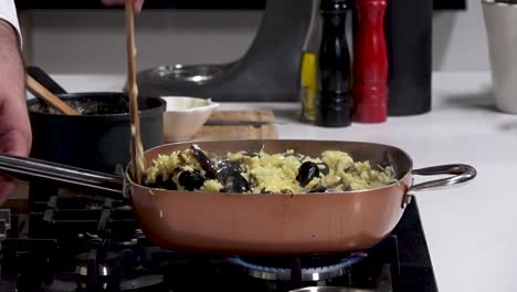 in a contemporary kitchen, fresh mussels are added to a creamy pasta dish, stirred together on a stovetop. aromas fill the air as dinner is prepared with care