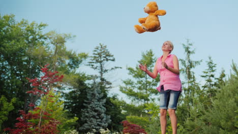 Frau-Mittleren-Alters,-Die-Spaß-Hat-Wie-Ein-Kind---Auf-Einem-Trampolin-Springen-Und-Einen-Teddybären-Hochwerfen