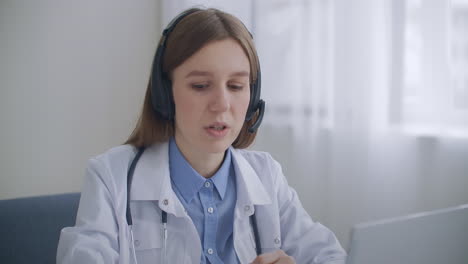 female head physician of hospital is communicating with doctors by online video conference at laptop sitting in her office