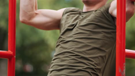 focused young athletic man doing pull-ups at red sports facility in park