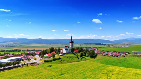 village view with distant peaks. lush countryside surrounds a picturesque village with a church tower under a bright blue sky during daytime