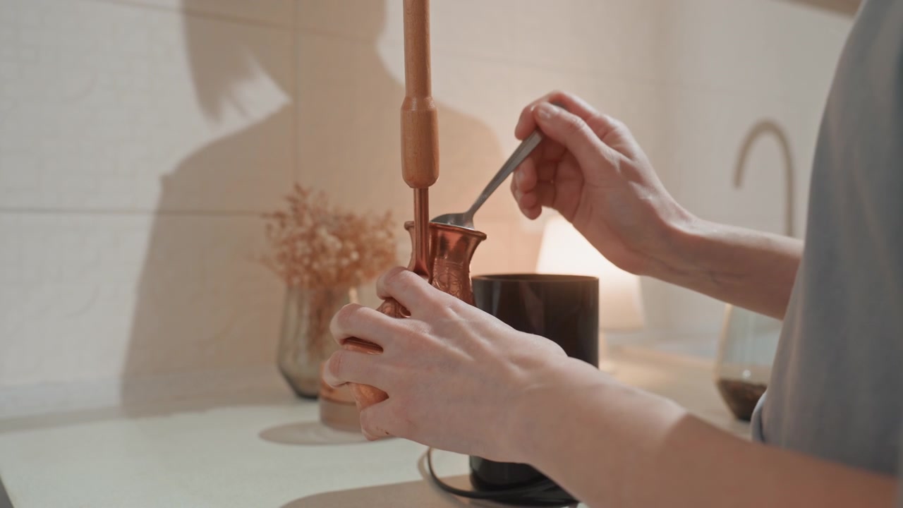 Mains blanches allumant une bougie près d'une cezve, une amatrice de café préparant un rituel matinal douillet sur le comptoir de la cuisine avec une cezve en cuivre et une bougie en cire d'abeille, une allumette frottée pour allumer une flamme chaleureuse, une douce lueur de lampe.