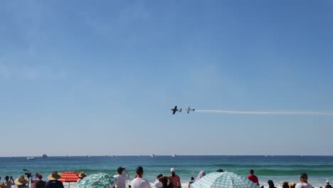 planes perform stunts over a busy beach scene