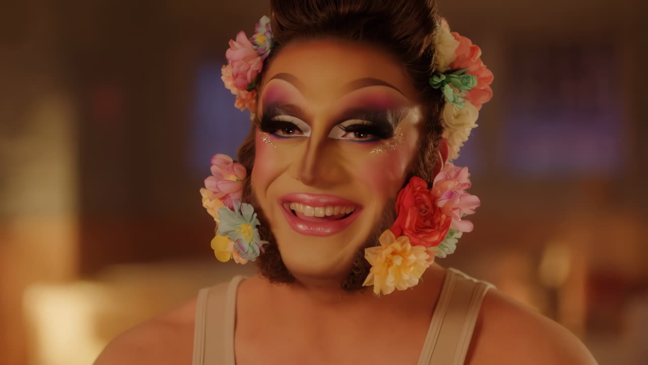 A close-up of a drag queen with elaborate makeup and flowers in their beard