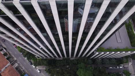 Drone-Volando-Hacia-Arriba,-Cerca-De-Un-Edificio-Con-Espejo-Simétrico,-La-Cámara-Apuntando-Hacia-Abajo-Revelando-El-Edificio-A-Medida-Que-Sube