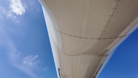 external view from the rear part of the lower part of a white color fuselage medium size jet, tilting down. sunny day with a blue sky. 4k