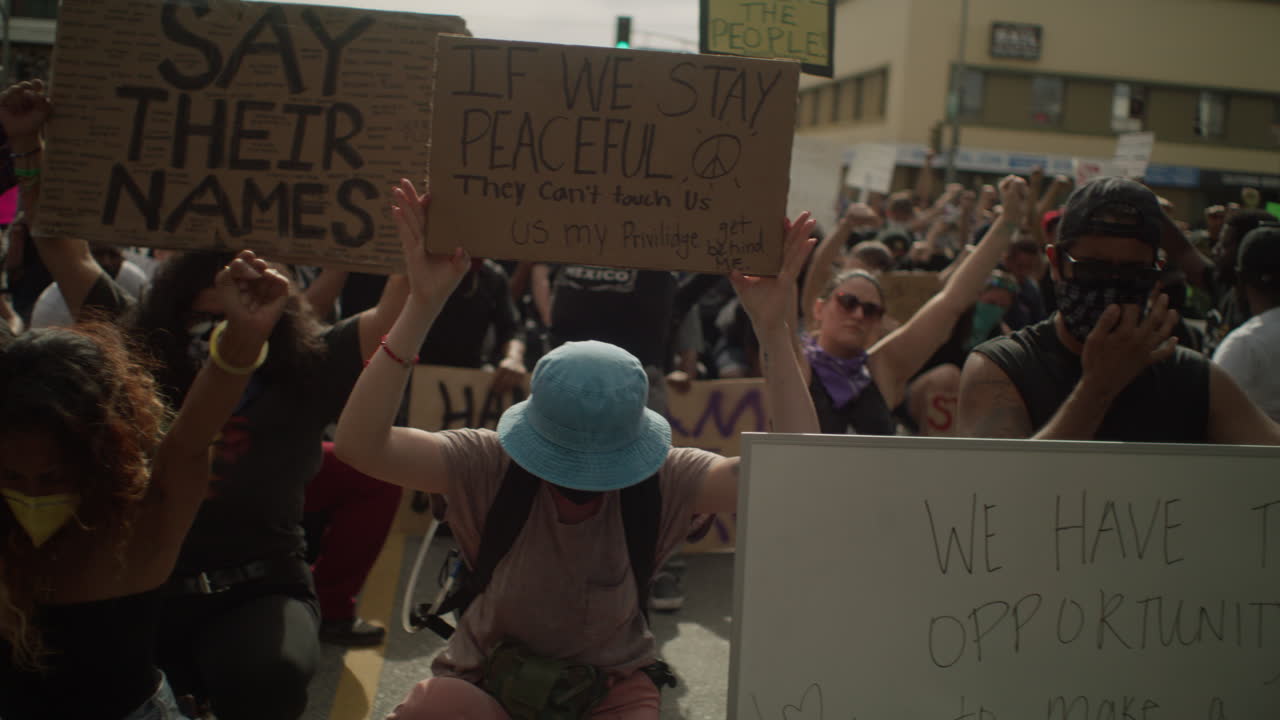 Group of protestors holding up multiple signs during a protest in front of police at the town hall
