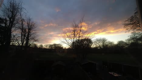 Fiery-red-sunset-clouds-passing-silhouette-autumn-garden-trees-time-lapse