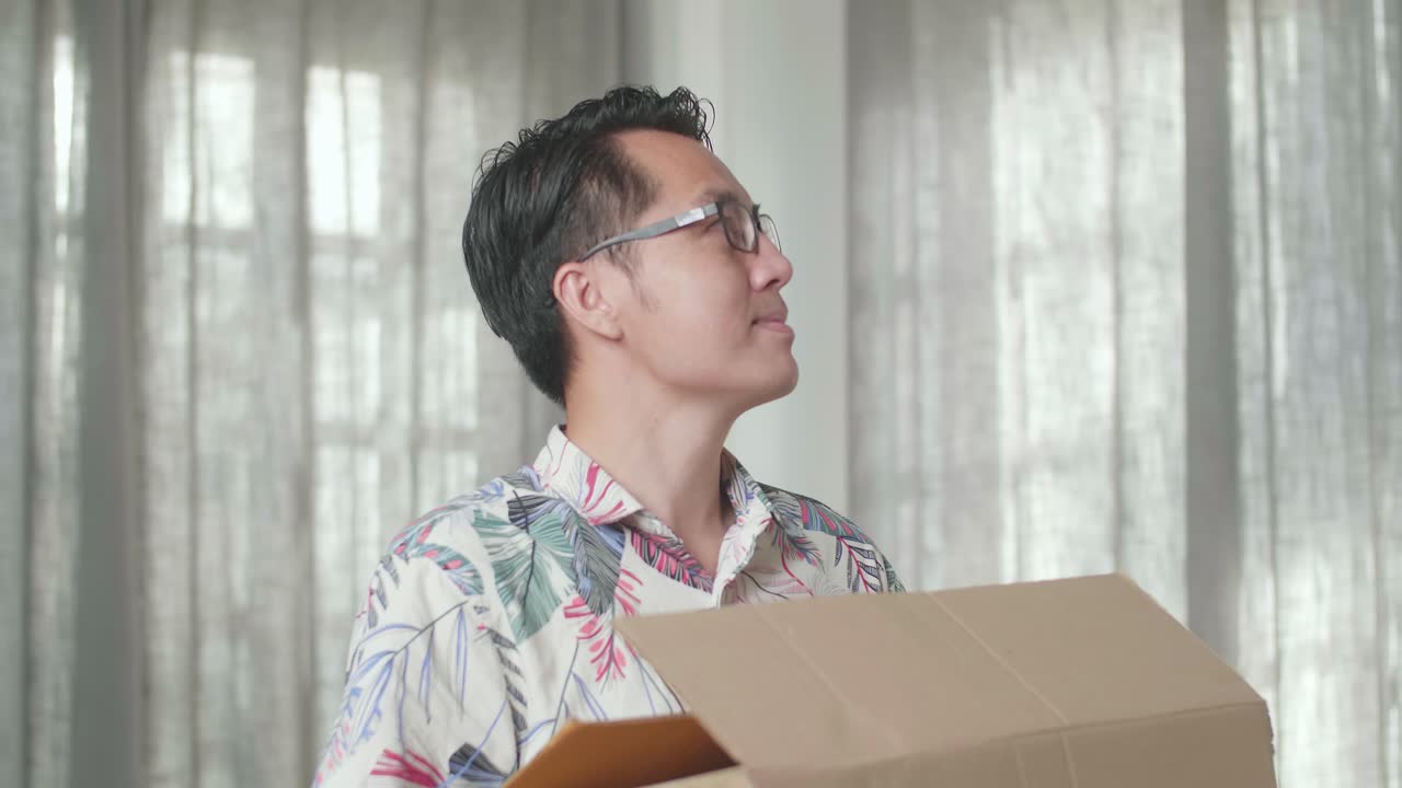 아시안 남자가 새로운 집으로 물건을 담은 카드보드 상자를 들고 주변을 둘러보며 새로운 집으로 이사합니다.