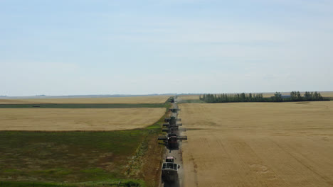 Toma-Aérea-Detrás-De-Cosechadoras-En-Saskatchewan,-Tierras-De-Cultivo-De-Canadá