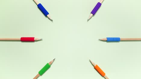 Top down stop motion of pencils with colored grips moving in a circle on pastel green, leaving center copy space