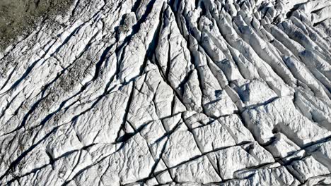 Aerial-flyover-over-Morteratsch-glacier-in-Engadin,-Switzerland-at-dawn-with-a-pan-up-towards-the-glacier-end-and-valley-covered-in-fog