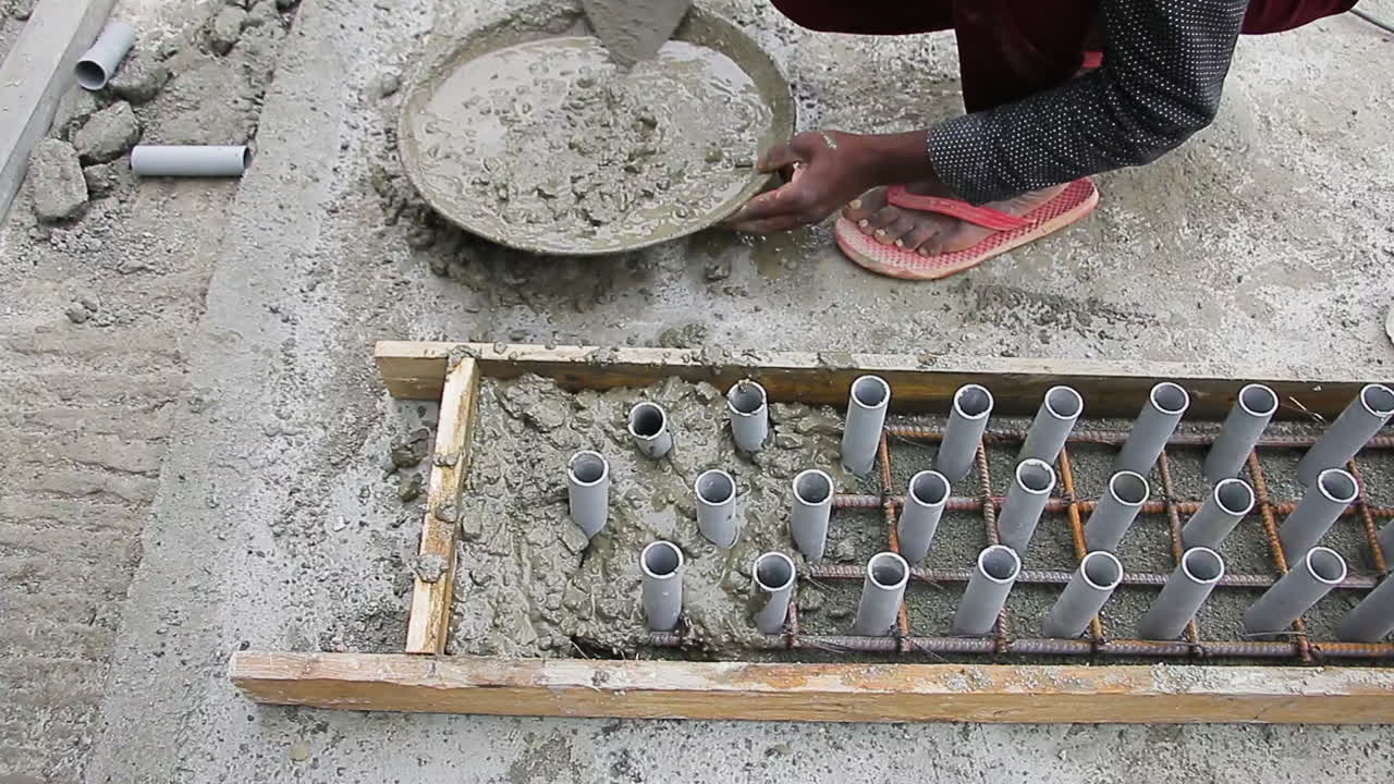 Indian mason worker placing and leveling wet concrete mix into a slab with pipes for construction