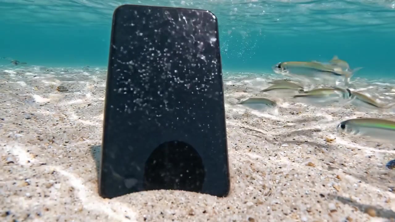 Ein Smartphone, das in klarem Wasser untergetaucht ist und eine faszinierende Szene aus Blasen und Sand erzeugt; die Schönheit der Unterwasserwelt und Technologie einfangend