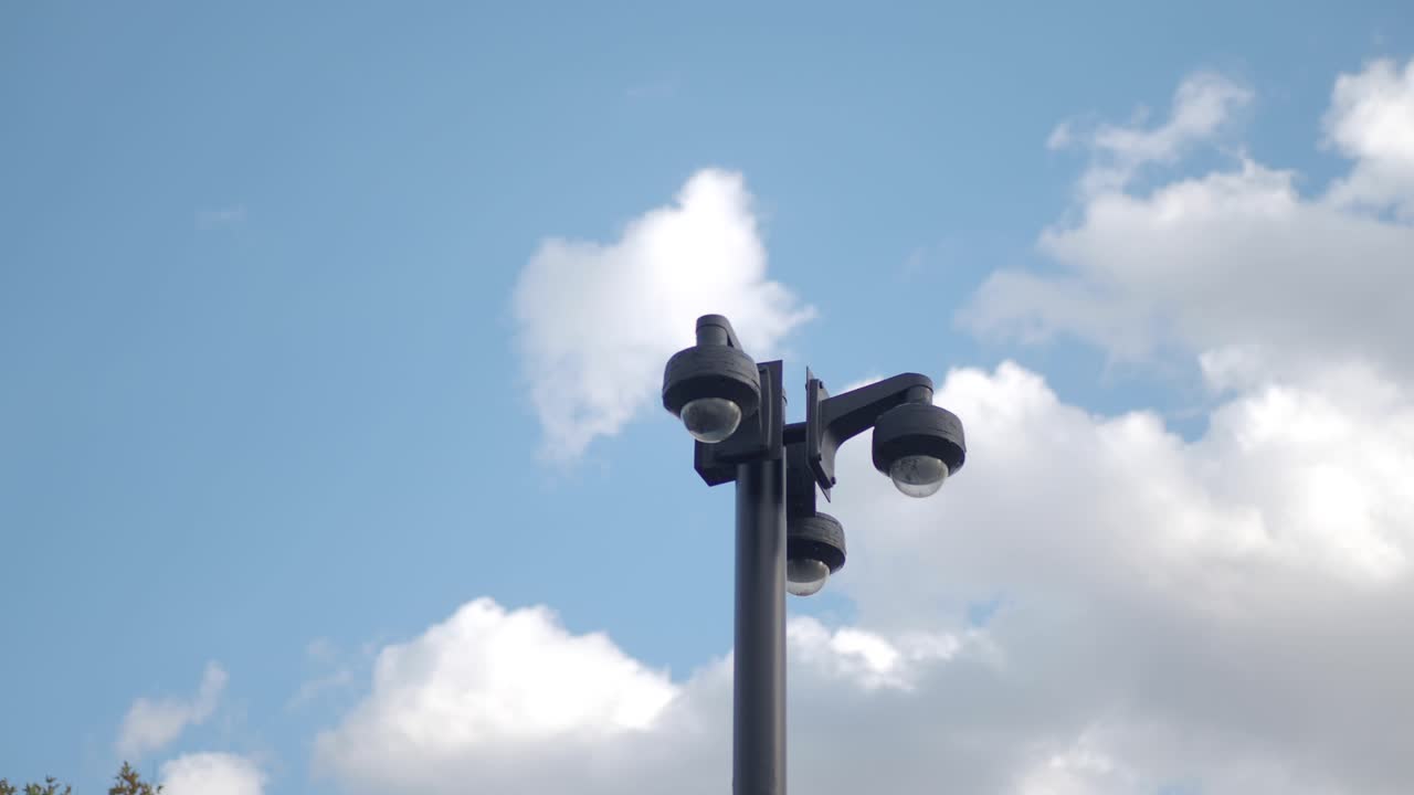 cámara de seguridad en un poste contra un cielo azul con nubes