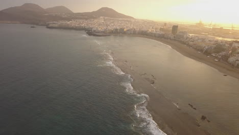 Fantastica-Toma-Aerea-De-Madrugada,-Mostrando-La-Barrera-Natural-De-La-Playa-Y-Mostrando-Tambien-La-Maravillosa-Playa-De-Las-Canteras-Y-Los-Edificios-De-La-Zona