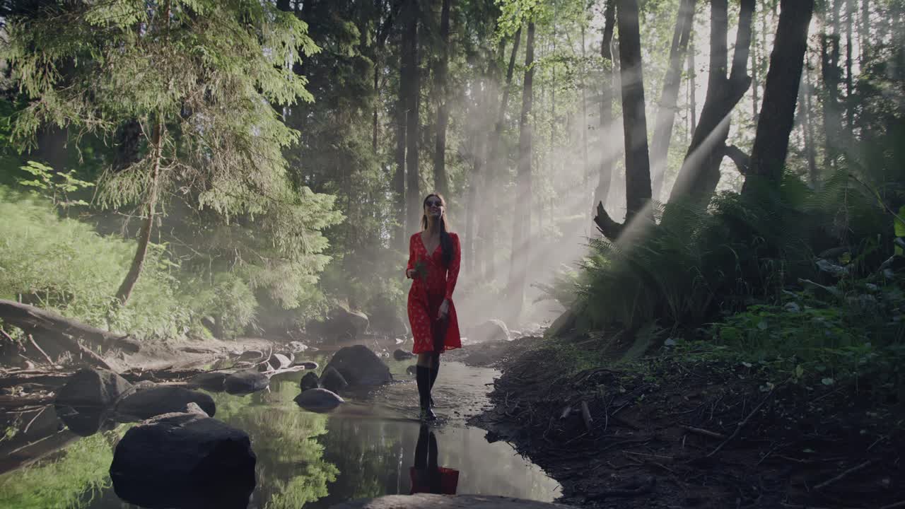 un paseo por el bosque encantado: una mujer con un vestido rojo vibrante caminando a lo largo de un lecho de un río a través de un exuberante bosque de cuentos de hadas en medio de la mística niebla y niebla de la mañana