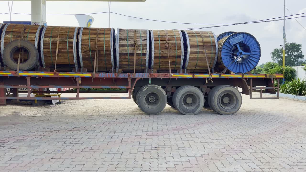Tilt-up shot of a flatbed truck loaded with large industrial wooden cable drums secured with straps, parked in a paved yard