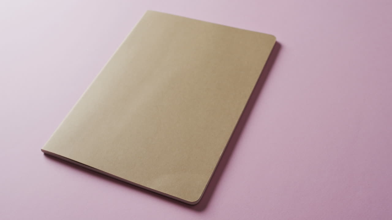 Close up of closed brown book with copy space on pink background in slow motion